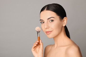 Poster - Beautiful young woman applying face powder with brush on grey background. Space for text