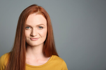 Candid portrait of happy young woman with charming smile and gorgeous red hair on grey background, space for text