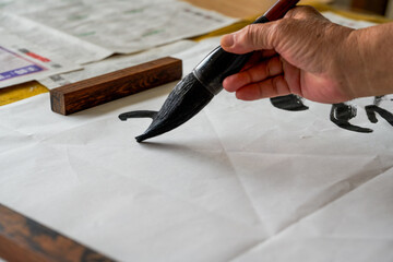 Wall Mural - a calligrapher is writing calligraphy characters with a large brush, a close-up of the brush. transl