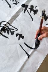 Wall Mural - a calligrapher is writing calligraphy characters with a large brush, a close-up of the brush. transl