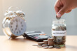 Hand putting Coins in glass jar with calculator and alarm clock for time to money saving for retirement concept ,  retirement planning.