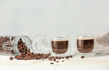 Glass cups of hot coffee with beans on light background