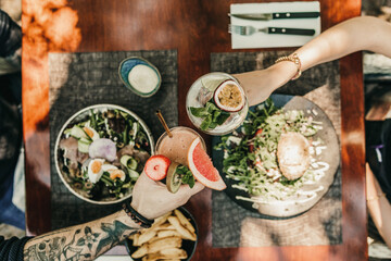 Wall Mural - People toasting with different alcoholic beverages on top of a table filled with culinary food in restaurant