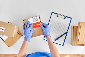 health protection, shipping and delivery concept - hands in gloves with returned parcel box and papers on clipboard