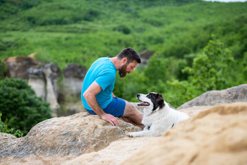 Wall Mural - man with his dog sitting on a rock enjoying nature