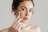 Fototapeta Konie - Half-naked brunette woman massaging face with jade roller