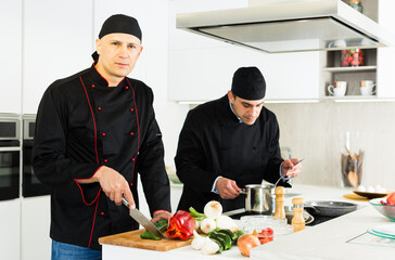 Two male cooks are making salad on their work place in the kitchen at the cafe.