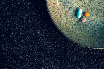 Wall Mural - Colored pills on a plate. Free space to write. Concept of replacing food with medication. Black background.