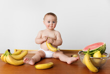 Adorable Baby Sitting On Kitchen Table Holding Banana