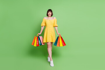 Canvas Print - Full body photo of attractive positive young woman hold hands shopping bags walk isolated on green color background