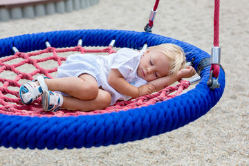 Wall Mural - Little toddler boy, sleeping in a round swing on a playground, tired after full day of games