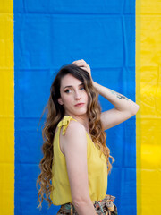 Wall Mural - Vertical closeup shot of a young attractive Caucasian female posing near a blue and yellow wall