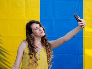 Wall Mural - Closeup shot of a young Caucasian female taking a selfie near a blue and yellow wall