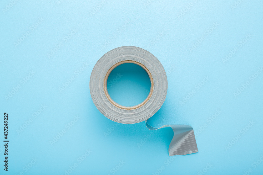One roll of silver cloth duct tape on light blue table background. Pastel color. Closeup. Top down view.