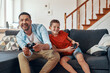 © gstockstudio - Happy young father and son playing video games while spending time at home