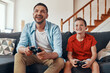 © gstockstudio - Happy young father and son playing video games while spending time at home