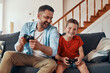 © gstockstudio - Happy young father and son playing video games while spending time at home
