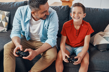 Wall Mural - Happy young father and son playing video games while spending time at home