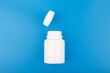 Top view of white opened medication bottle against blue background. Concept of medications, sleeping pills or vitamins and supplements