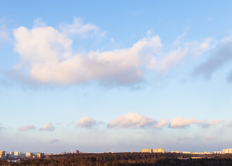 Wall Mural - fluffy clouds in blue sunset sky over city park