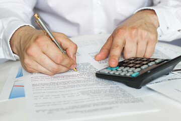 A businessman sitting at an office desk signs a contract with a shallow emphasis on signing. business and finance