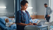 © Gorodenkoff - Hospital Ward: Professional Smiling Black Female Head Nurse or Doctor Wearing Stethoscope Uses Medical Computer. In the Background Patients in Beds Recovering Successfully after Sickness and Surgery