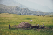 Beautiful Foggy Mountain Landscape With Scarecrow On Wooden Fence Around Haystack On Background Of Mountains And Rocks Silhouettes In Fog. Stack Of Hay Is Surrounded By Wood Fence In Vintage Tones.