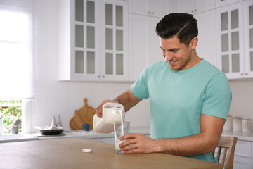 Canvas Print - Man pouring milk from gallon bottle into glass at wooden table in kitchen