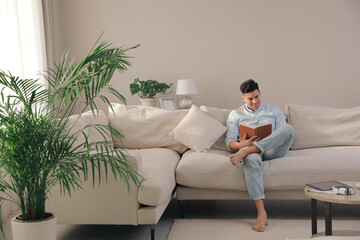 Canvas Print - Man reading book on sofa in living room