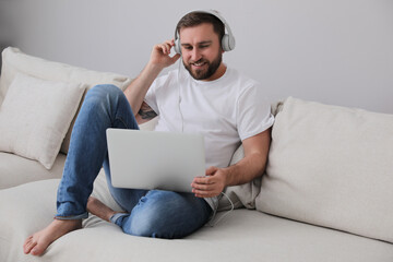 Wall Mural - Man with laptop and headphones sitting on sofa at home