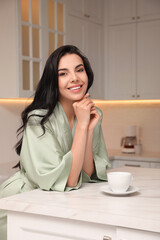 Wall Mural - Pretty young woman wearing beautiful silk robe with cup of coffee in kitchen
