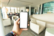 © Travel Wild - (Copy space) Overhead view of an human hand holding a smart phone with a white screen in an airport lounge. Concept of showing information on a mobile phone during Covid-19 pandemic.