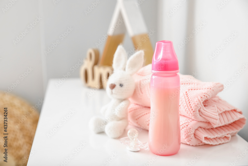 Bottle of milk for baby with toy and clothes on shelf