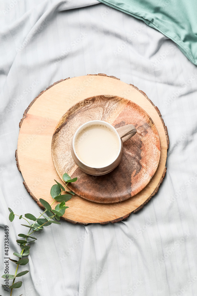 Wooden board with cup of coffee on bed