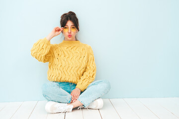 Wall Mural - Young beautiful smiling female in trendy summer hipster clothes. Sexy carefree woman posing near light blue wall in studio. Positive model having fun indoors. Cheerful and happy