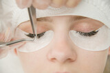 Fototapeta  - Close up beautiful young woman during eyelash extension. Top down view