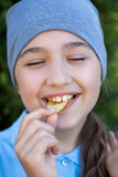 Fototapeta  - Portrait Of Happy Little Smiling Russian Girl Eyes Potato Chips In Park Outdoors.