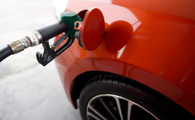 Green benzene gas pump nozzle filling up orange sport car tank. Close up