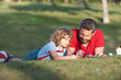 © Olena - father and son relax on grass in park learning to draw, fatherhood
