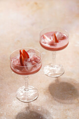 Two glasses with red strawberry dessert with ice cubes and crashed ice and strawberry slices