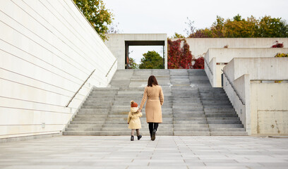 family, motherhood, love and care concept - back view of mother and her little daughter walking in city park