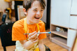 © Iryna - Cute positive happy boy with down syndrome sitting in a chair and drawing with paintbrush indoor.
