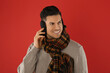 Man wearing stylish earmuffs and scarf on red background