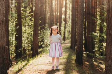 A cute little girl in glasses in nature on a sunny day