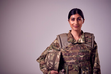 Studio Portrait Of Smiling Young Female Soldier In Military Uniform Against Plain Background