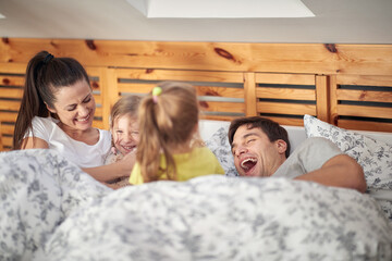 A young happy family having fun while is laying in the bed at home together. Family, together, love, home