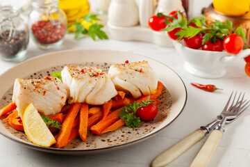 Wall Mural - Fried pieces of cod loin, served with sweet potato fries. Light stone background.