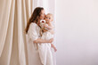 © Antipina - Mom hugs baby on a white background. Eco parenting concept. White clothes and a diaper  natural fabrics linen cotton muslin.  Mother's love. Hugs, smiles, happiness. Mother and child togetherness