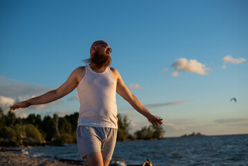 Wall Mural - A humorous portrait of a brutal man in a T-shirt and boxers on the beach at sunset