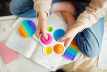 Teenage girl playing with rainbow pop-it fidget toy while studying at home. Teen kid with trendy stress and anxiety relief fidgeting game.